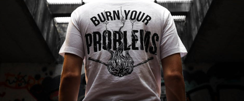 Person wearing a white t-shirt with 'Burn Your Problems' text and graphic, standing in an urban setting.